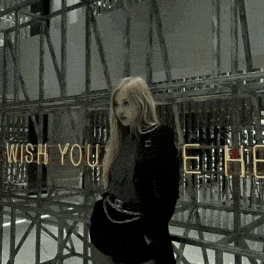 a woman stands in front of a sign that says wish you were here