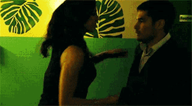 a man and a woman are standing next to each other in front of a green wall