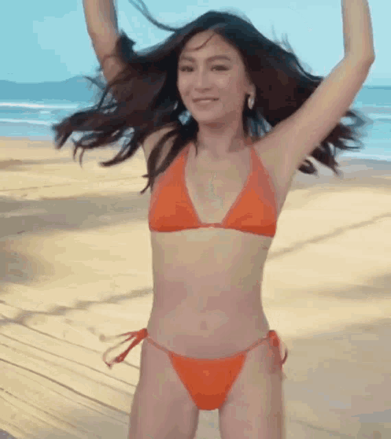 a woman in an orange bikini is dancing on a beach .