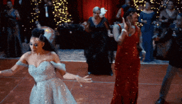 a woman in a silver dress is dancing with two other women in red dresses