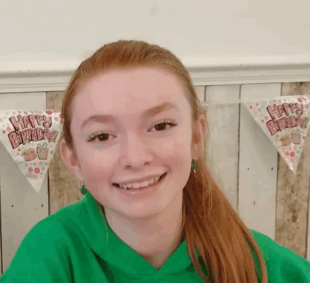 a girl in a green shirt is smiling in front of a banner that says happy birthday