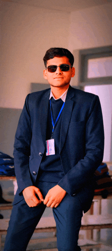 a man in a suit and sunglasses has a name tag around his neck that says ' aditya ' on it