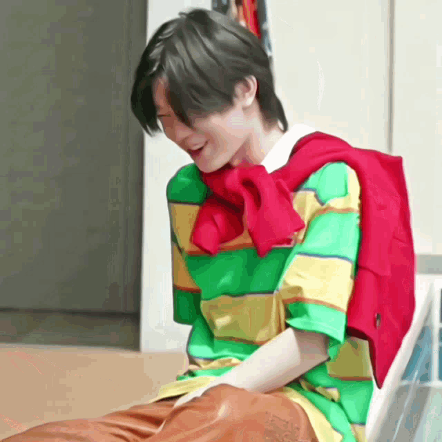 a man wearing a green yellow and red striped shirt with a red sweater around his neck