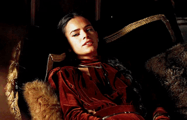a woman in a red velvet dress is sitting in a chair and smiling .