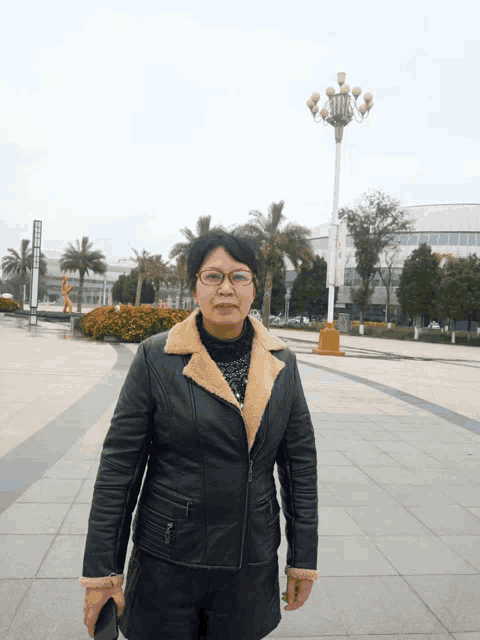 a woman wearing glasses and a black leather jacket stands in front of a street light