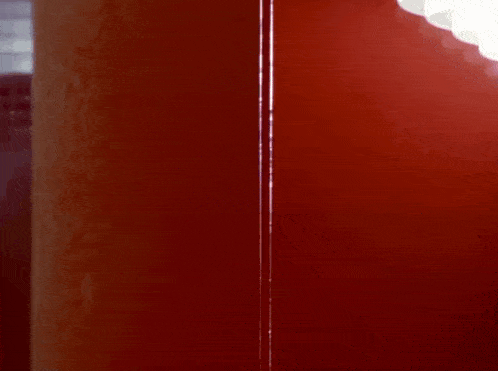 a man wearing a purple hat and a purple coat is peeking out from behind a red wall .