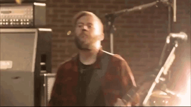 a man with a beard is playing a guitar and singing into a microphone on a stage .