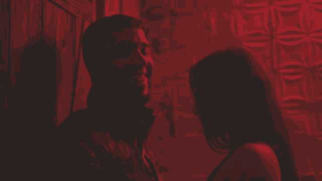 a man and a woman are looking at each other in a red room