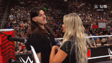 a man with a mustache stands next to a woman in a wrestling ring with usa written on the screen behind them