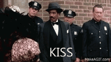 a man in a tuxedo and hat is standing in front of a group of police officers and a woman .