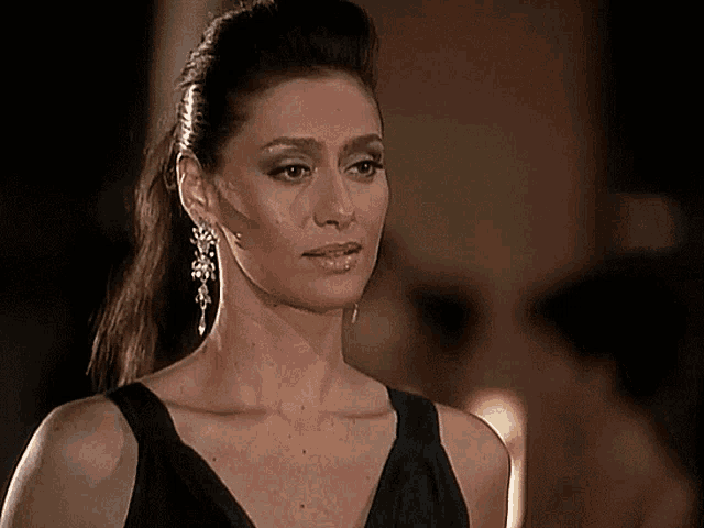 a woman wearing a black dress and earrings looks serious