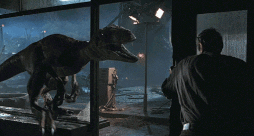 a man looks out a window at a dinosaur in the dark
