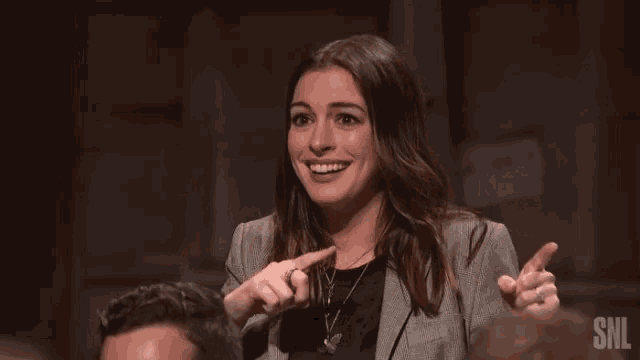 a woman is raising her hands in the air while sitting in a snl audience .