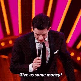 a man in a tuxedo is holding a microphone and says give us some money