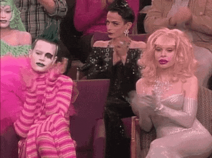 a group of drag queens are sitting in a theatre clapping .