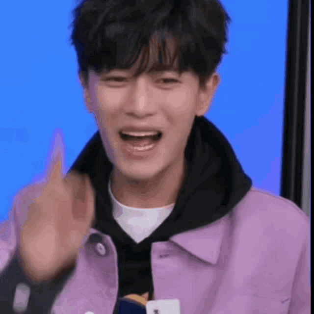 a young man in a purple jacket is smiling and waving .
