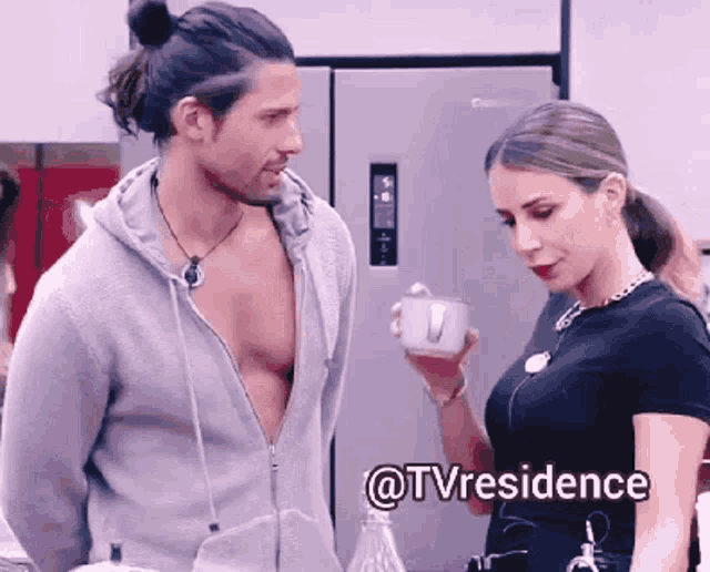 a man and a woman are standing next to each other and the woman is holding a cup and the man is shirtless