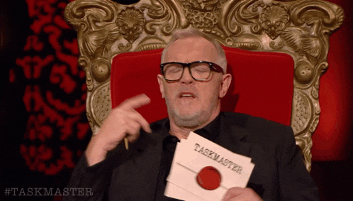 a man sitting in a chair holding a piece of paper that says taskmaster on it