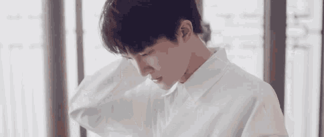 a young man in a white shirt is standing in front of a window and looking down .