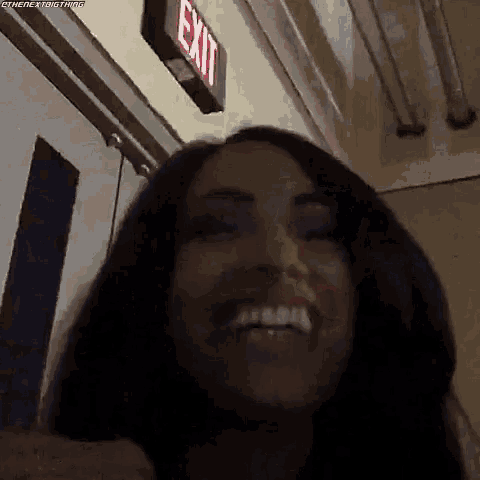 a woman is smiling in front of an exit sign in a hallway .