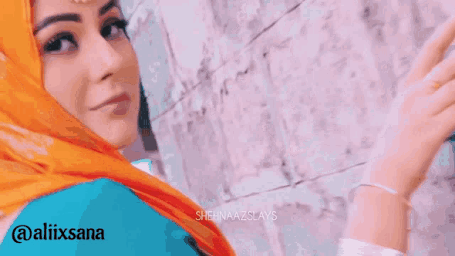 a woman wearing an orange scarf and a blue shirt is standing in front of a brick wall ..
