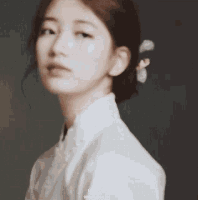 a close up of a woman 's face wearing a white shirt and a bun .