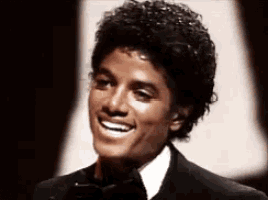 a young man in a tuxedo and bow tie smiles at the camera