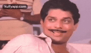 a man with a mustache is smiling while sitting on a couch .