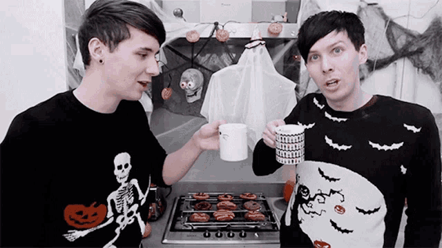 two men wearing halloween sweaters are standing next to each other drinking coffee