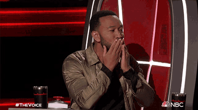 a man covering his mouth with his hands while sitting at a table with nbc written on it