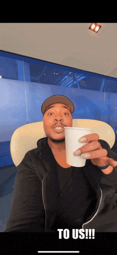a man sitting in a chair holding a cup that says " to us " on it