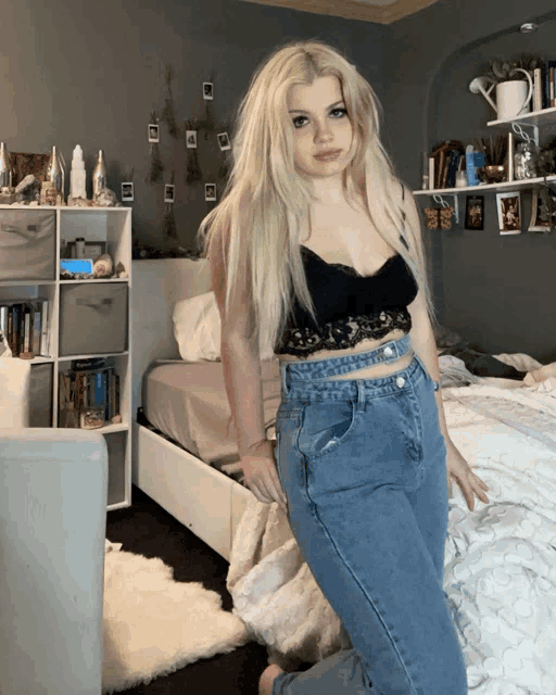 a woman in a black top and blue jeans stands in a bedroom