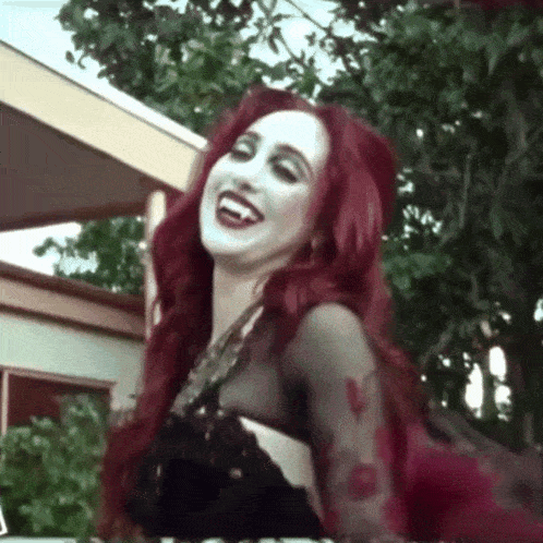 a woman with red hair and white paint on her face is wearing a black dress .