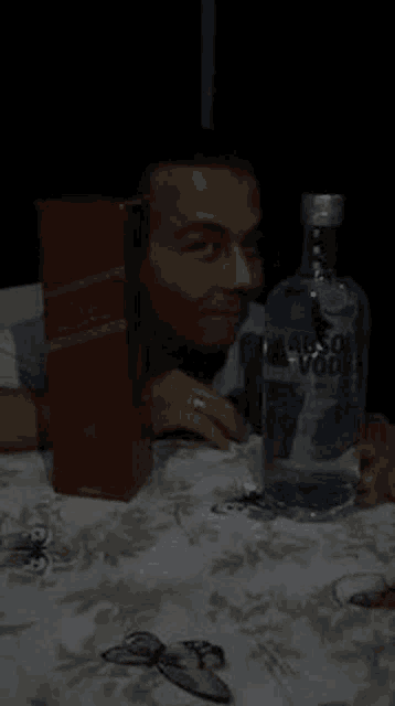 a man is sitting at a table with a bottle of absolut vodka and a box of whiskey .