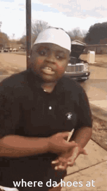a man wearing a polo shirt and a white hat is standing on a sidewalk and says where da hoes at