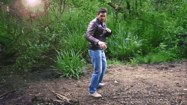 a man in a leather jacket and jeans is standing in a forest