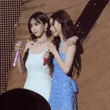 two women are standing next to each other on a stage and one is holding a microphone