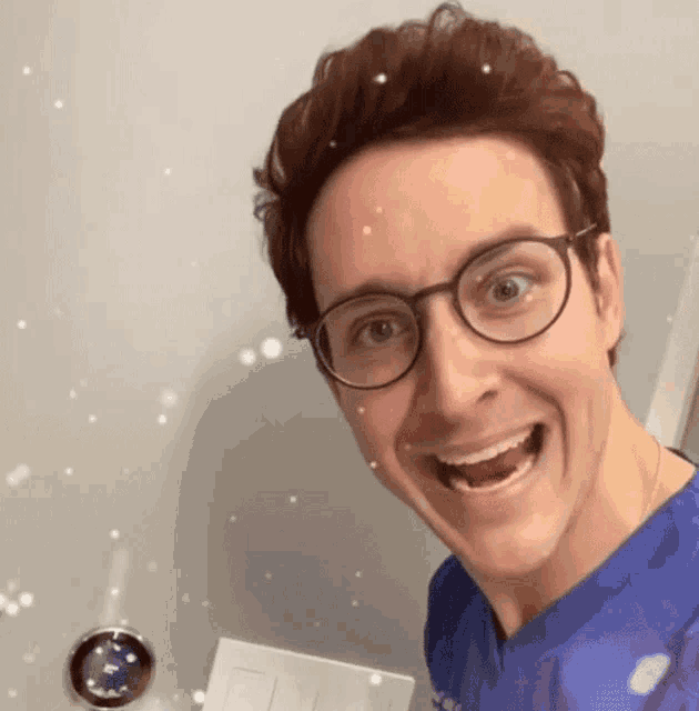 a man wearing glasses and a blue scrub top is smiling and making a funny face .