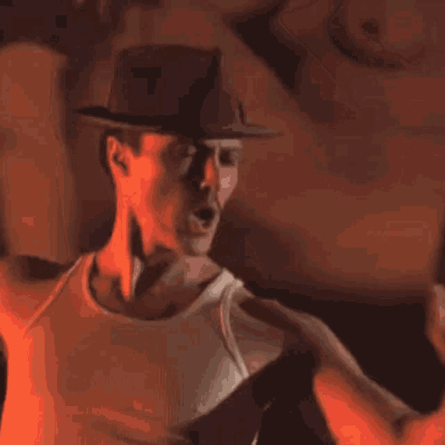 a man wearing a hat and a tank top is dancing in a dark room .