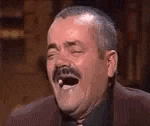 a man with a mustache is laughing with his mouth open in a suit and tie .