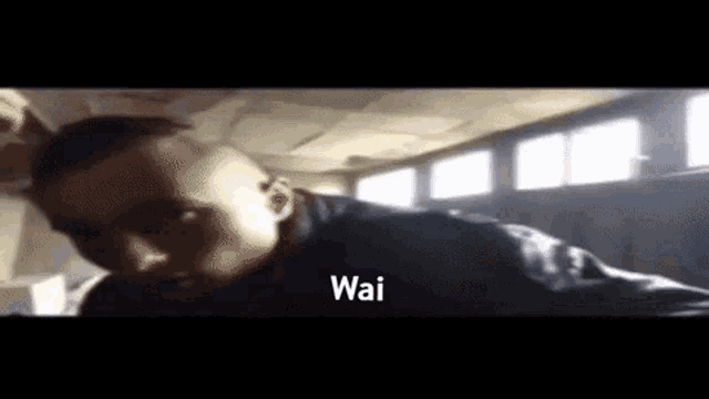 a man in a black shirt is standing in a dark room with the word wai written on the bottom .