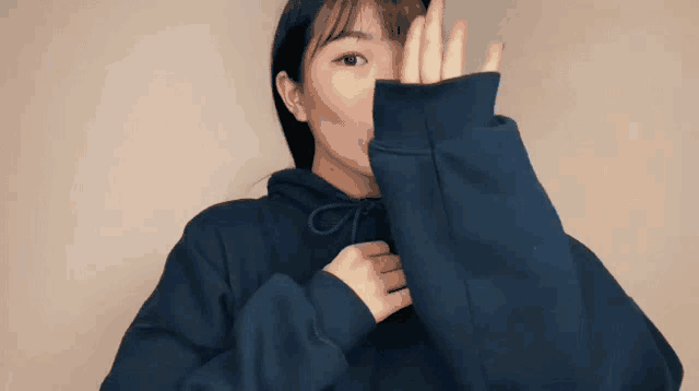 a woman wearing a blue hoodie is covering her face with the hood .