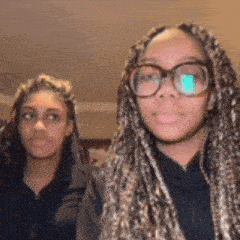 two girls wearing glasses and braids are standing next to each other in a room .