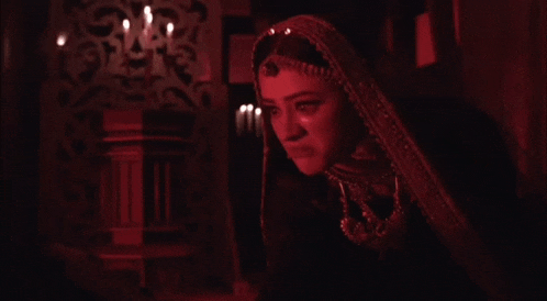 a woman in a red veil is standing in a dark room with candles in the background