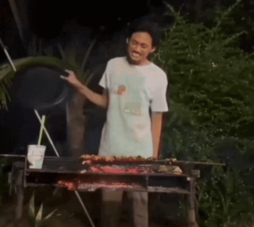 a woman covering her mouth while standing in front of a barbecue