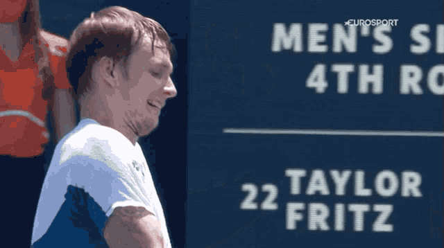 a man stands in front of a sign that says men 's tennis 4th round 22 taylor fritz