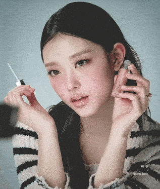 a woman is holding a bottle of lip gloss and a brush