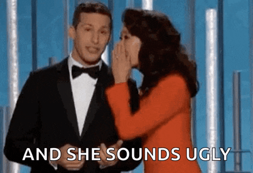 a man in a tuxedo is being whispered into a woman 's ear while she covers her mouth .