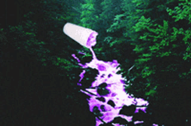 a cup of purple liquid is being poured into a stream