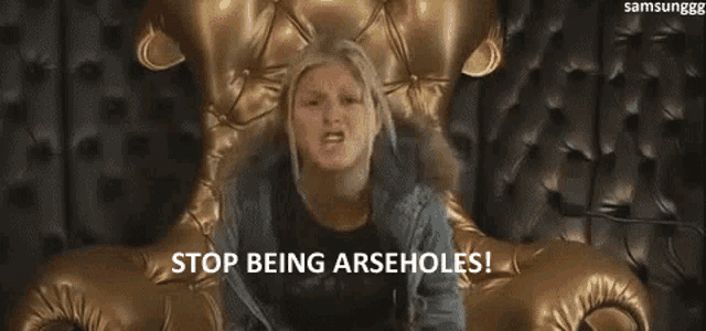 a woman is screaming while sitting on a gold couch and says `` stop being arseholes ! ''